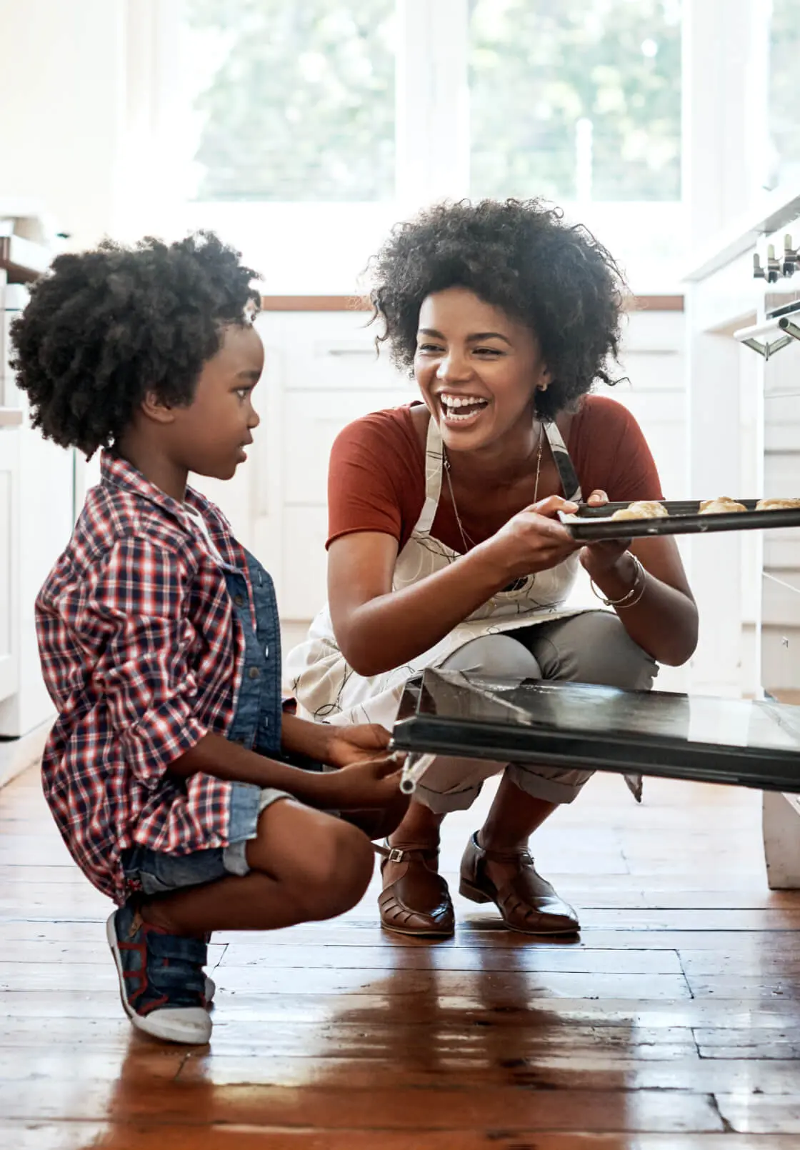 A mother and daughter smile and laugh while putting cookies in the oven, grateful for the appliance financing that let them afford the new range.