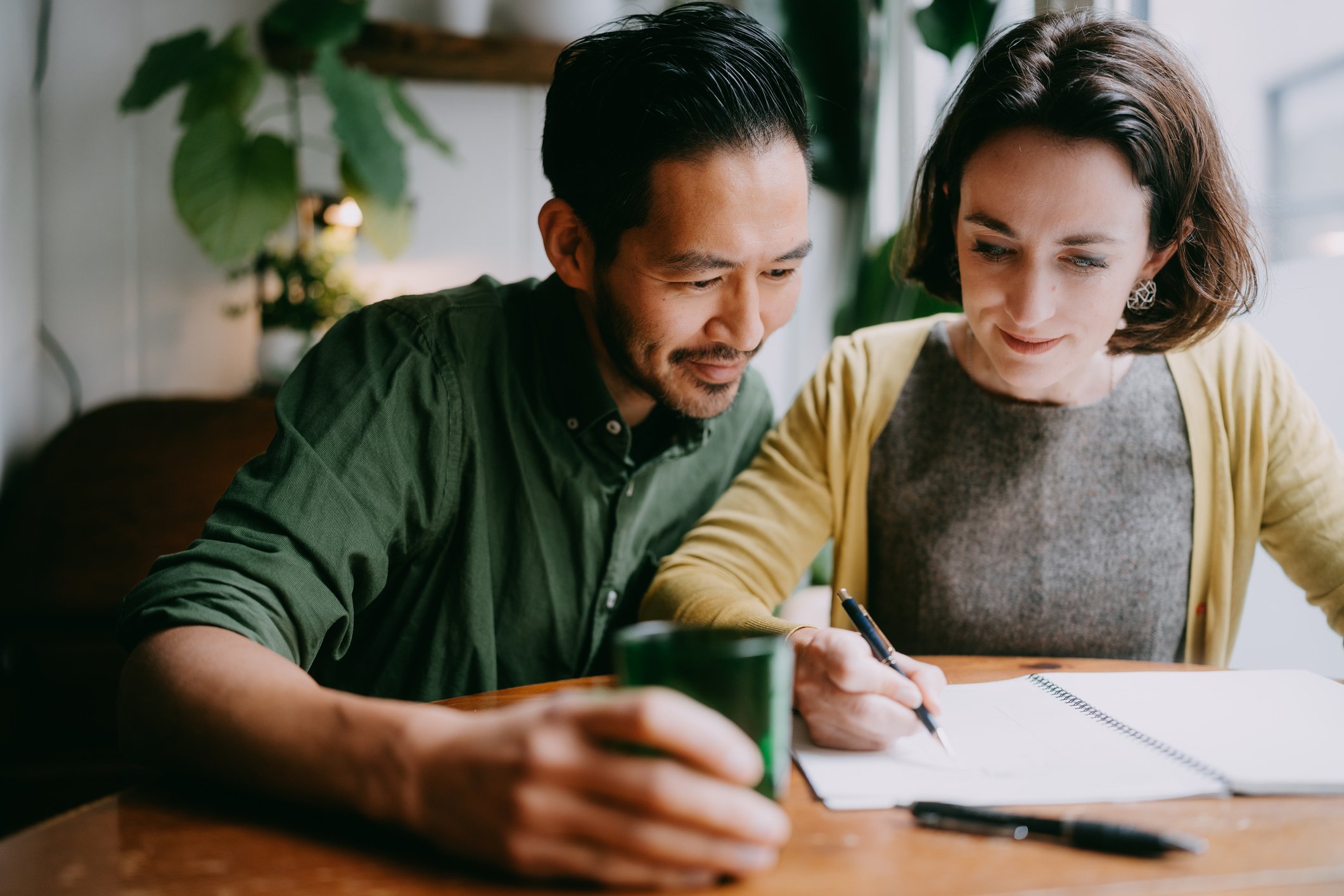 Couple sitting next to each other, apparently planning with pens and notepads