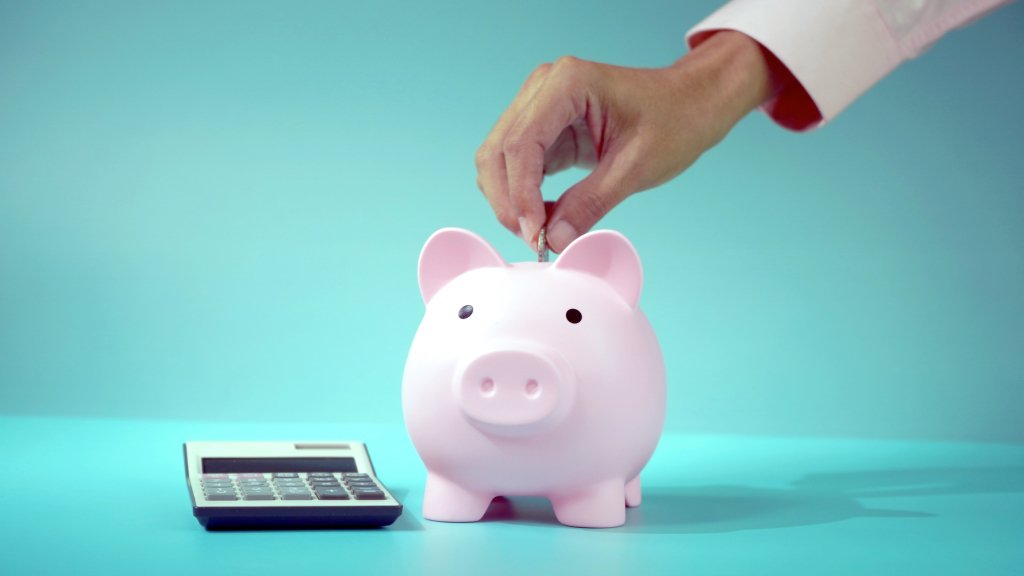 Person putting coin into a piggy bank with a calculator next to it